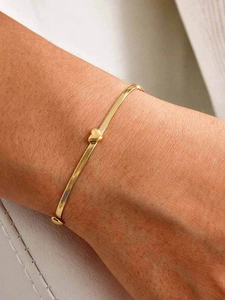 Gros plan d'un bracelet en maille serpent dorée avec un pendentif cœur poli sur un poignet
