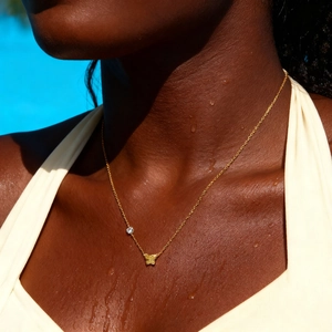 Nahaufnahme der goldenen Schmetterlingskette mit Zirkon am Hals einer Frau am Pool
