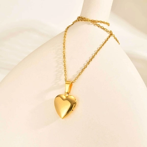 Detail of a gold heart locket necklace with hinge structure on white ceramic stand