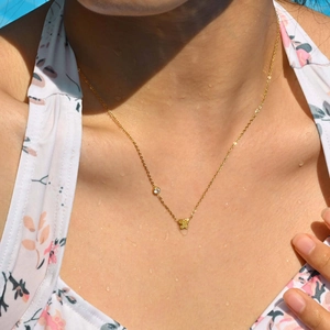 Goldene Halskette mit Schmetterlingsanhänger und Zirkon auf Haut im Sonnenlicht