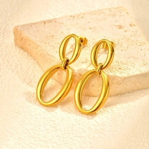 Detailed close-up of polished gold oval link earrings on a textured stone surface