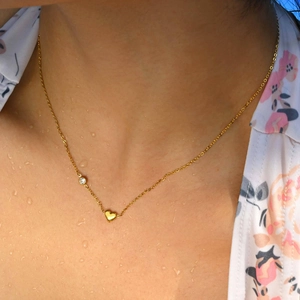 Nahaufnahme einer goldenen Herzanhänger-Halskette mit Zirkonia am Hals eines Models