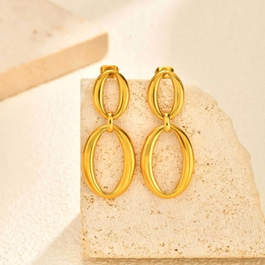 Close-up of polished gold-plated double oval drop earrings on a stone display stand
