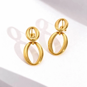 Close-up of polished gold oval geometric earrings on a white minimalist pedestal