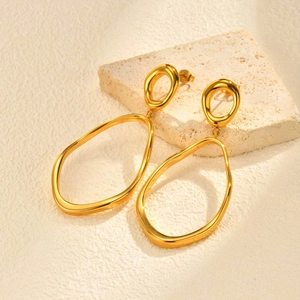 Boucles d'oreilles pendantes géométriques dorées sur un présentoir en pierre minimaliste