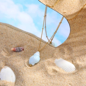 Close-up of ocean-style ceramic conch necklace with golden beads on a beach mirror
