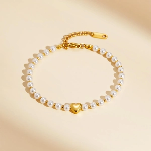 Détail du pendentif cœur doré sur bracelet en perles blanches avec fermoir en métal doré