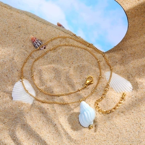 Golden bead chain necklace with white seashell pendant on a sandy beach setting