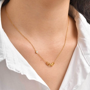 Détail de pendentifs ovales dorés entrelacés et d'un zircon sur collier minimaliste