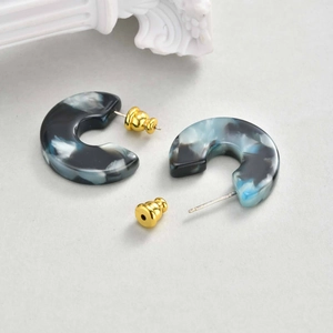 Macro detail of C-shaped marble resin earrings with elegant golden spherical metal backs