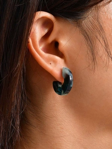Detail of C-shaped acrylic earring with green and grey marble texture on a model