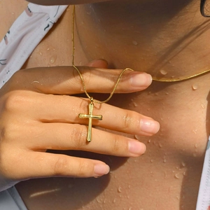 Détail d'un collier avec pendentif croix dorée sur un mannequin avec des gouttes d'eau