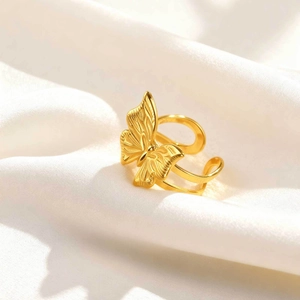 Detailed close-up of golden stainless steel butterfly ring on white silk fabric