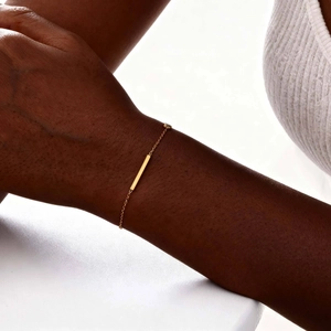 Gros plan d'un bracelet barre dorée minimaliste porté au poignet avec finition polie