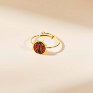 Vista detallada de un anillo de mariquita con esmalte rojo sobre banda dorada ajustable