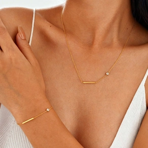 Parure minimaliste en acier doré avec barre et zircon portée au cou et au poignet