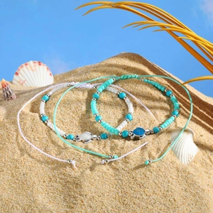 Detail of adjustable ocean-style turquoise beaded anklets with turtle charms on a beach