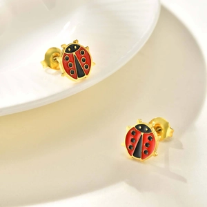 Primer plano de pendientes de mariquita dorados con esmalte rojo y negro en plato blanco