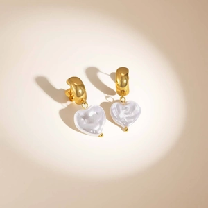 Detail of heart-shaped pearl drop earrings with polished gold-plated stainless steel hoops