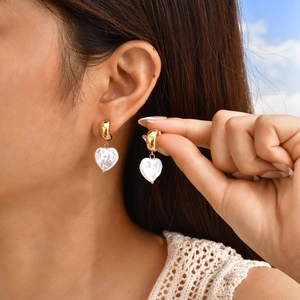 Close-up of elegant gold hoop earrings with marbled white heart charms on model