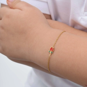 Detalle de una delicada pulsera de cadena dorada con un pequeño dije de flor de tulipán