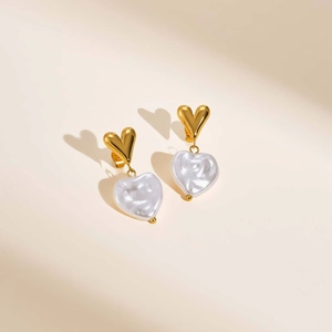 Detail view of 18k gold heart earrings with elegant white pearl-like heart pendants