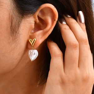 Detail shot of heart-shaped pearl drop earrings in 18k gold finish worn by a model