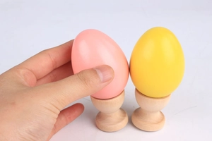 Detailed view of hand holding colorful wooden toy eggs with natural wood egg cups