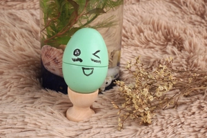 Detail of mint green egg-shaped toy with a cute face on a natural wood base stand