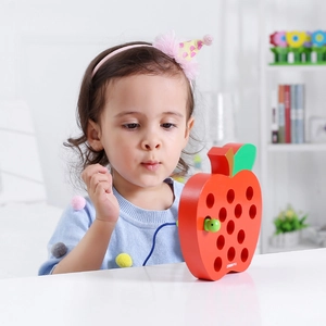 Close-up of a child playing with a red wooden apple threading toy for motor skills