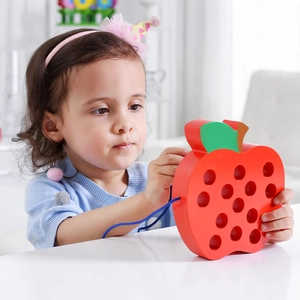 Close-up of a child practicing fine motor skills with wooden apple lacing toy