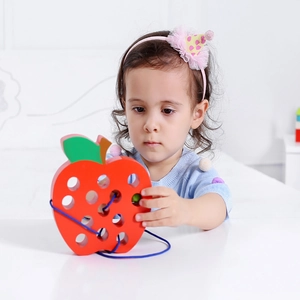 Close-up of a child playing with a red wooden apple threading toy for fine motor skills