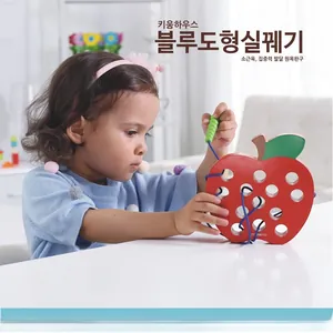Toddler practicing hand-eye coordination with a wooden apple lacing toy in a cozy setting