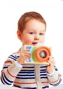 Detail of wooden toy camera with colorful prism lens held by a young child on white background
