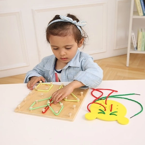 Toddler girl practicing fine motor skills with wooden lacing board and geometric geoboard