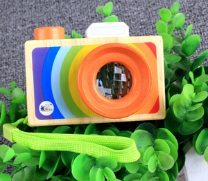Macro detail of wooden toy camera with rainbow sticker and orange lens on green leaves