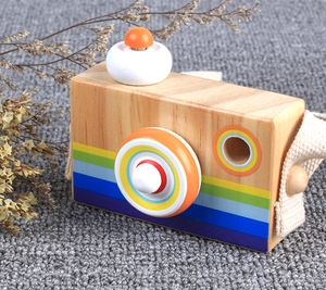 Detail of wooden toy camera with rainbow patterns and canvas strap on a grey carpet