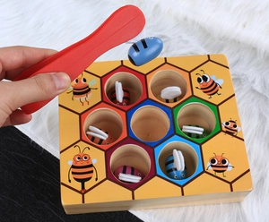 Detail of wooden bee hive game showing colorful bees and tweezers for motor skills training