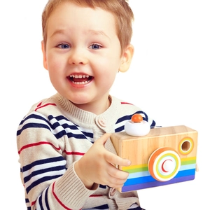Child hands holding a wooden toy camera with colorful stripes and kaleidoscope lens