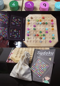 Detailed view of the wooden Sudoku game board set with colorful numbered pegs and manual