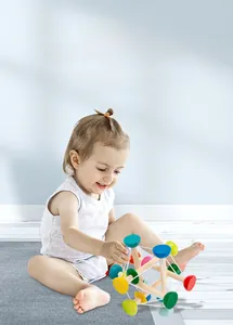 Close-up of baby hand grasping the colorful elastic sensory wooden toy on soft carpet