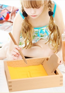 Detail of child using wooden Montessori sand tray with stylus for writing practice