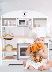 Toddler using a white and wood play kitchen featuring a microwave, sink, and oven