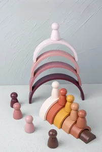 Close-up of stacking wooden rainbow arches and small peg dolls in soft Morandi colors