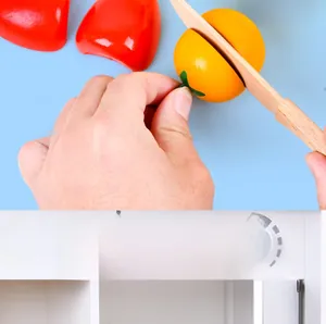 Close-up of wooden toy vegetables with velcro and a white play kitchen storage cabinet