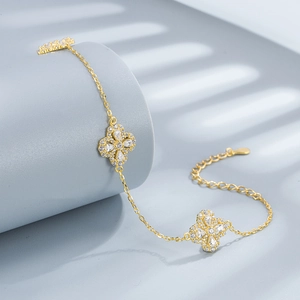 Elegant gold clover bracelet with sparkling zircons on a blue aesthetic background