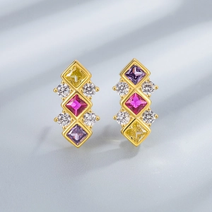 Close-up of geometric gold earrings with vertical yellow, rose and purple square crystals
