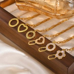 Set of six gold stainless steel chains with heart, floral, and shell pendants on silk fabric