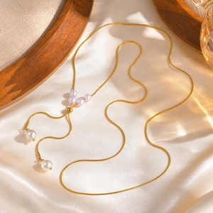 Collier en Y élégant en maille serpent dorée avec perles posé sur du satin blanc