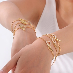 Detailed layered gold bracelet set with heart charms and OT toggle clasp on wrist
